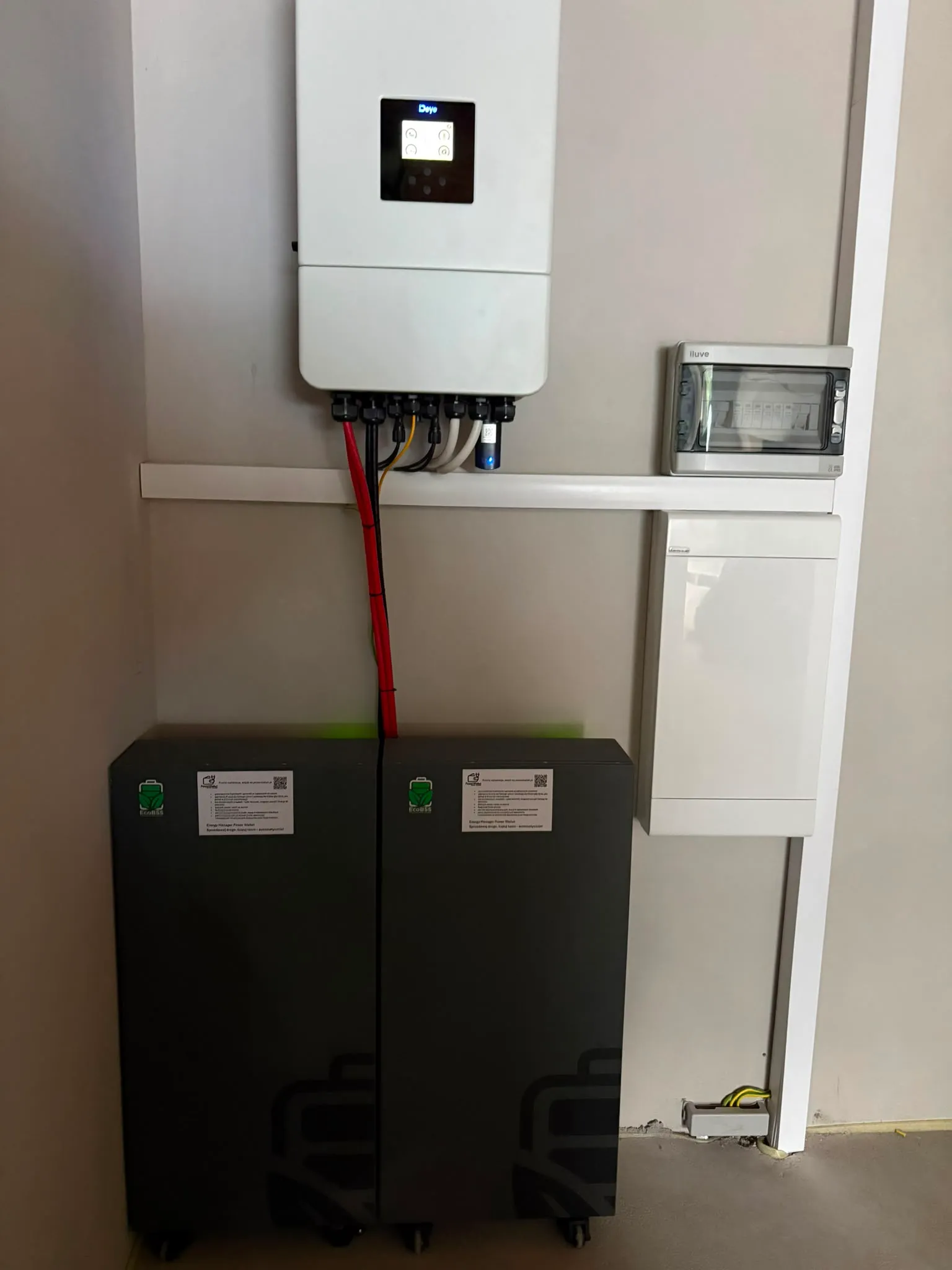 Falownik hybrydowy Deye na ścianie, pod nim dwa moduły magazynu energii EcoBSS